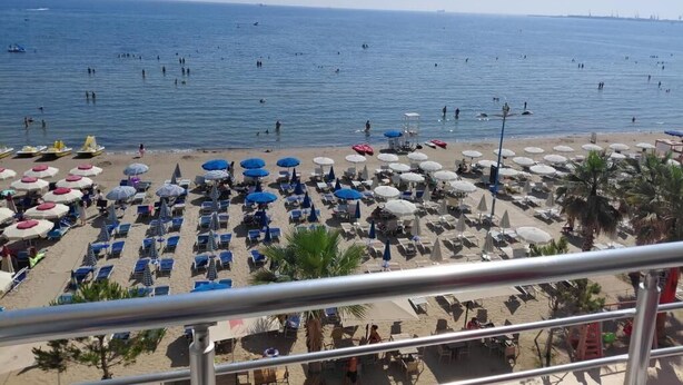 Una playa con numerosos sombrillas y tumbonas, cielo despejado y el mar al fondo.