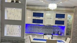 Una sala de estar moderna con un sofá, un comedor con mesa y sillas, y una cocina con un salpicadero iluminado en azul.