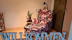 A room with a floral-patterned armchair, a small table with a plant, and a 'WILLKOMMEN' sign. - Your vacation address in the beautiful, hilly Teutoburg Forest (Extertal)