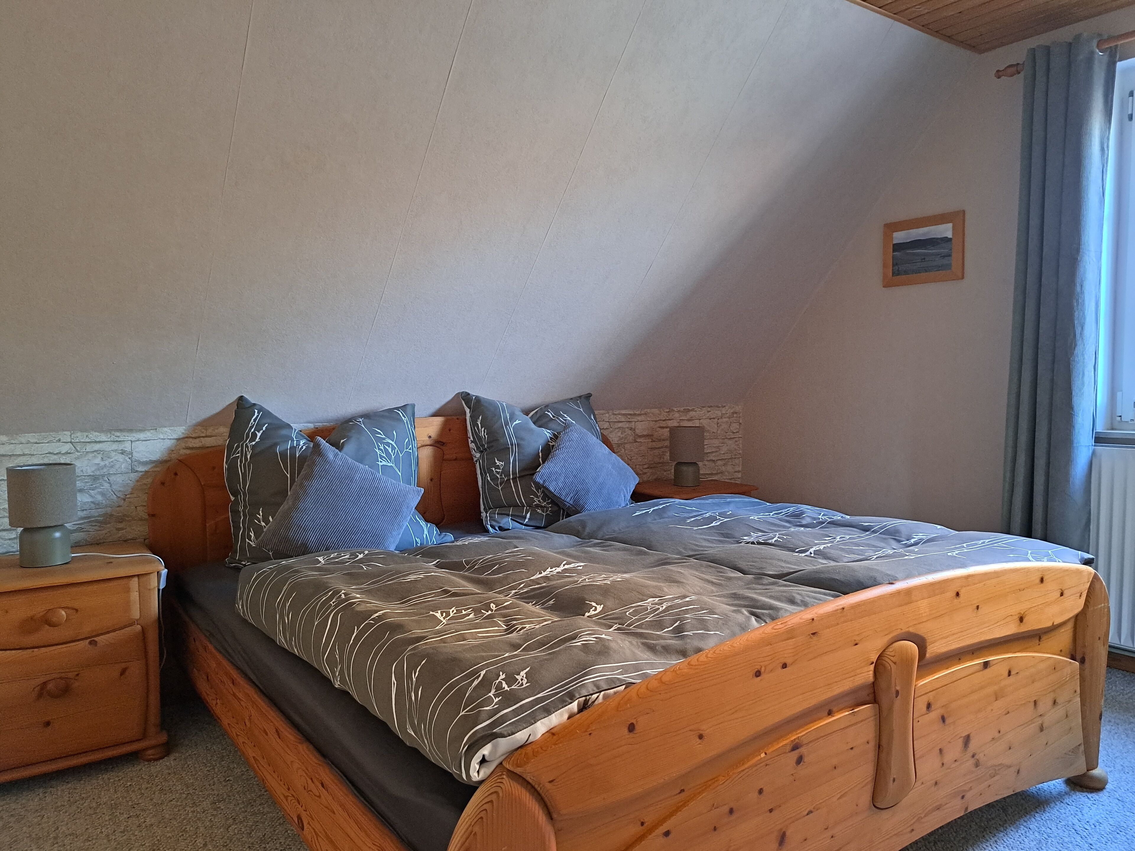 A bedroom with a wooden bed, a nightstand, a lamp, and a stone wall.