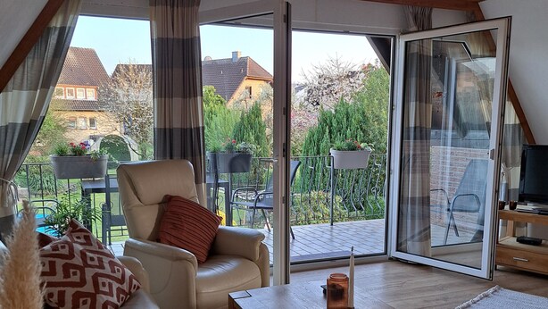 A cozy living room with a sofa, coffee table, and a view of a garden and neighboring houses through large glass doors. - Your vacation address in the beautiful, hilly Teutoburg Forest (Extertal)