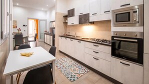 Una cucina moderna con mobili bianchi, piano cottura a gas, forno a microonde e forno. C'è un tavolo da pranzo con sedie e un tappeto colorato.