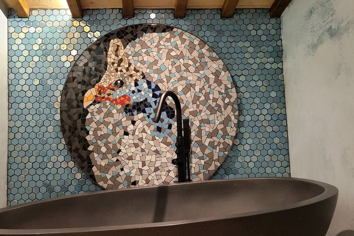 Casa de banho com parede em mosaico, banheira e área de duche.