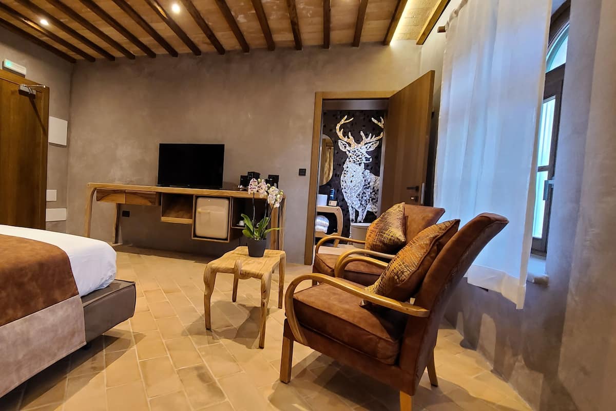 Quarto de hotel com cama, escrivaninha, cadeira e televisão.