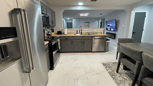 A modern kitchen with stainless steel appliances, a central island, and a dining area with a gray table and chairs.