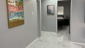 A hallway with a marble floor leading to a bedroom with a bed and a nightstand.