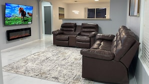 A modern living room with a flat-screen TV, leather recliners, a patterned rug, and a fireplace.
