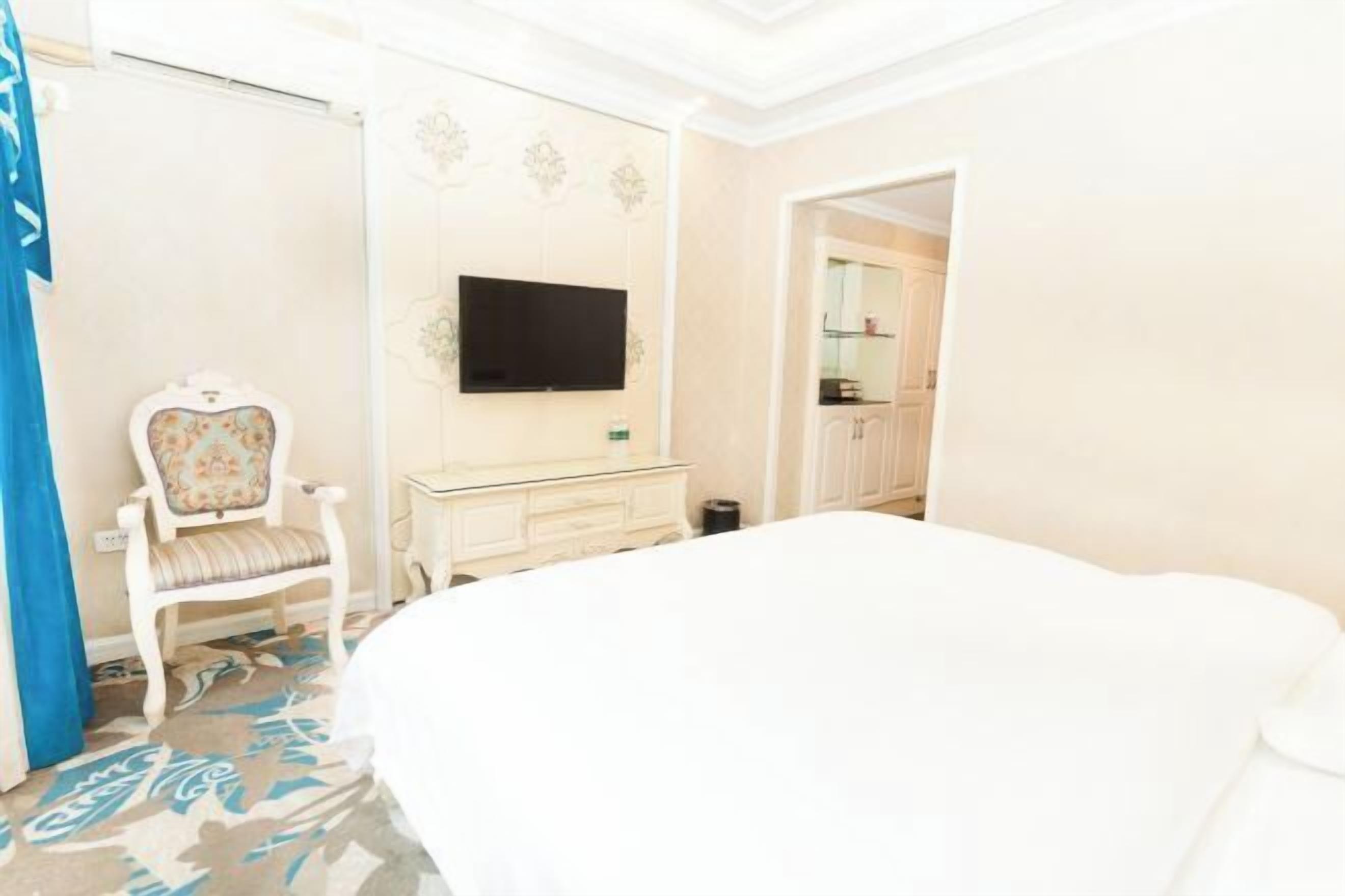 Una habitación de hotel con una cama grande, televisión montada en la pared, tocador con espejo y una silla.