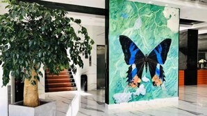 Eine Lobby mit einem großen Kunstbaum, einem Empfangsbereich und einer Wandkunst mit Schmetterlingen.
