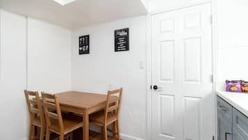 A dining area with a wooden table and chairs, a white door, and two black wall art pieces.
