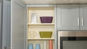 Eine Küche mit grauen Schränken, einem Edelstahlbackofen und diversen Küchenutensilien in Regalen.