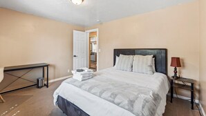 A bedroom with a bed, bedside table, lamp, and a desk with a chair. - Charming Mountain Retreat with Enclosed Backyard and Artistic Flair (Millcreek)