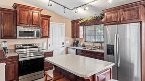 A modern kitchen with wooden cabinets, stainless steel appliances, a granite countertop, and a window with blinds. - Charming Mountain Retreat with Enclosed Backyard and Artistic Flair (Millcreek)