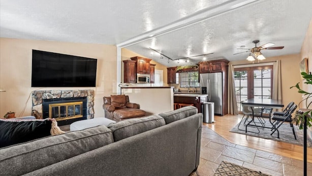 A spacious living room with a gray sectional sofa, a stone fireplace, and a flat-screen TV mounted on the wall. - Charming Mountain Retreat with Enclosed Backyard and Artistic Flair (Millcreek)