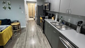 A modern kitchen with grey cabinets, stainless steel appliances, and a wooden floor.