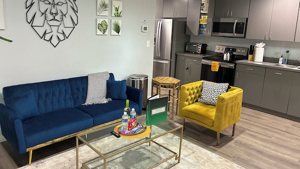 A modern living room with a blue sofa, a yellow armchair, and a glass coffee table.