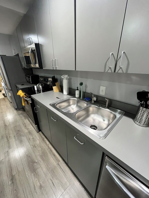 Una cocina moderna con armarios grises, un lavamanos doble y electrodomésticos de acero inoxidable.