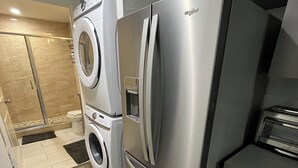 A compact kitchen with a stainless steel refrigerator, a washing machine, and a small countertop with a toaster.