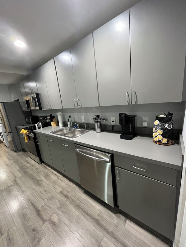 A modern kitchen with grey cabinets, stainless steel appliances, and a wooden floor.