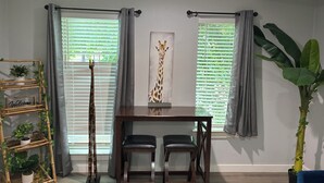 A dining area with a table, chairs, a giraffe painting, and a bamboo plant shelf.