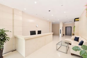 A reception area with a reception desk, two chairs, a clock, a plant, and a sofa with a glass coffee table. - Dong'an Business Hotel (Guilin University of Technology Pingfeng Campus Branch) (Guilin)