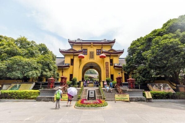 Un bâtiment traditionnel de couleur jaune, doté d’une arche centrale, entouré de verdure et accessible par un escalier.