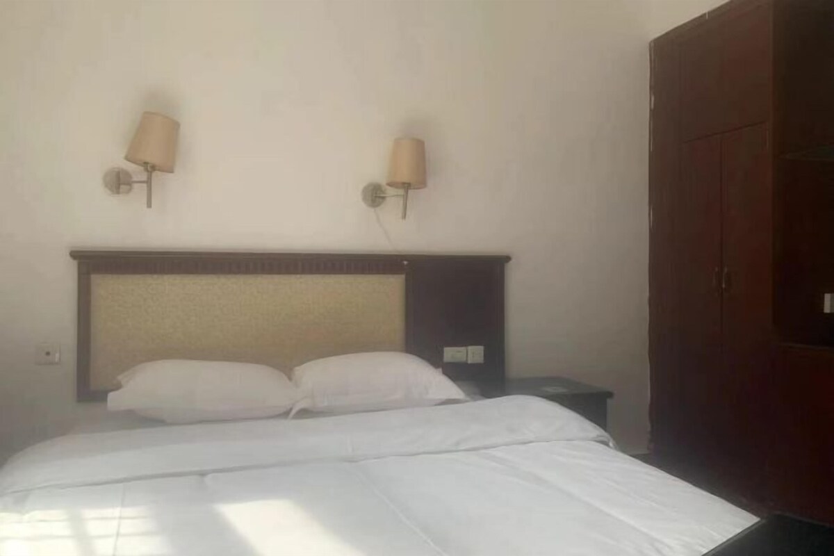 A hotel room with a bed, two wall-mounted lamps, a wardrobe, and a nightstand.