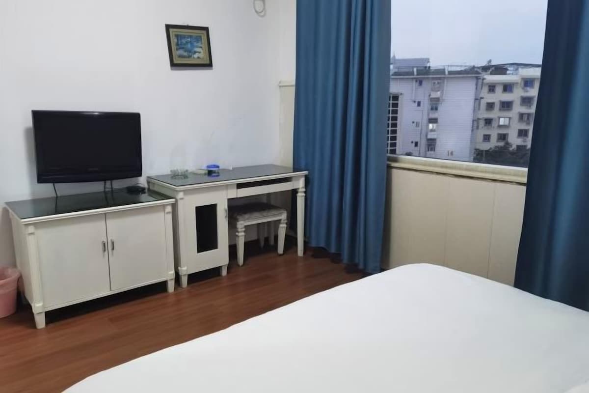 A hotel room with a bed, a desk with a television, a small table, and a window with curtains.