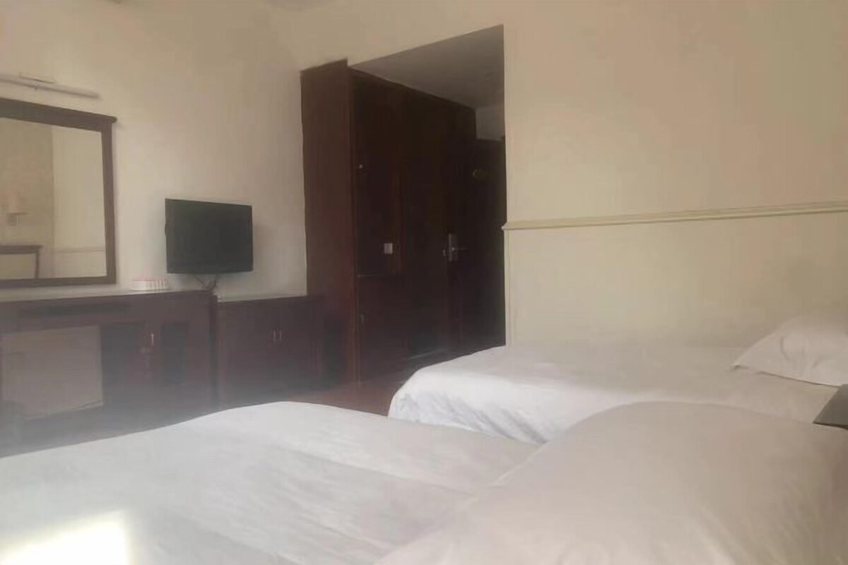 A hotel room with two beds, a desk with a flat-screen TV, a mirror, and a wardrobe.