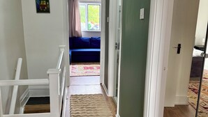 A hallway with a wooden staircase, a blue sofa, and a beige rug. - The Walthamstow Lodge (London)