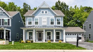 Une maison à deux étages avec un porche à l’avant, un garage et une pelouse bien entretenue.