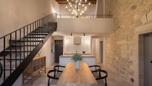 Un interior moderno con una mesa de comedor de madera, sillas negras, una escalera y una pared de piedra.