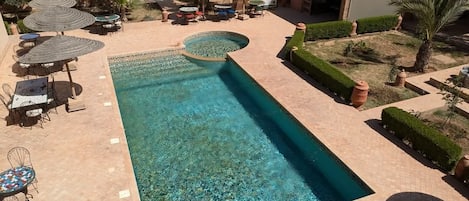 A swimming pool with a tiled deck, surrounded by outdoor seating and umbrellas.