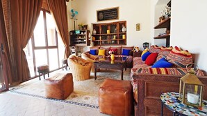 A cozy living room with a sofa set, ottomans, a coffee table, and a bookshelf. - Riad dar chenguiti (Taroudant)