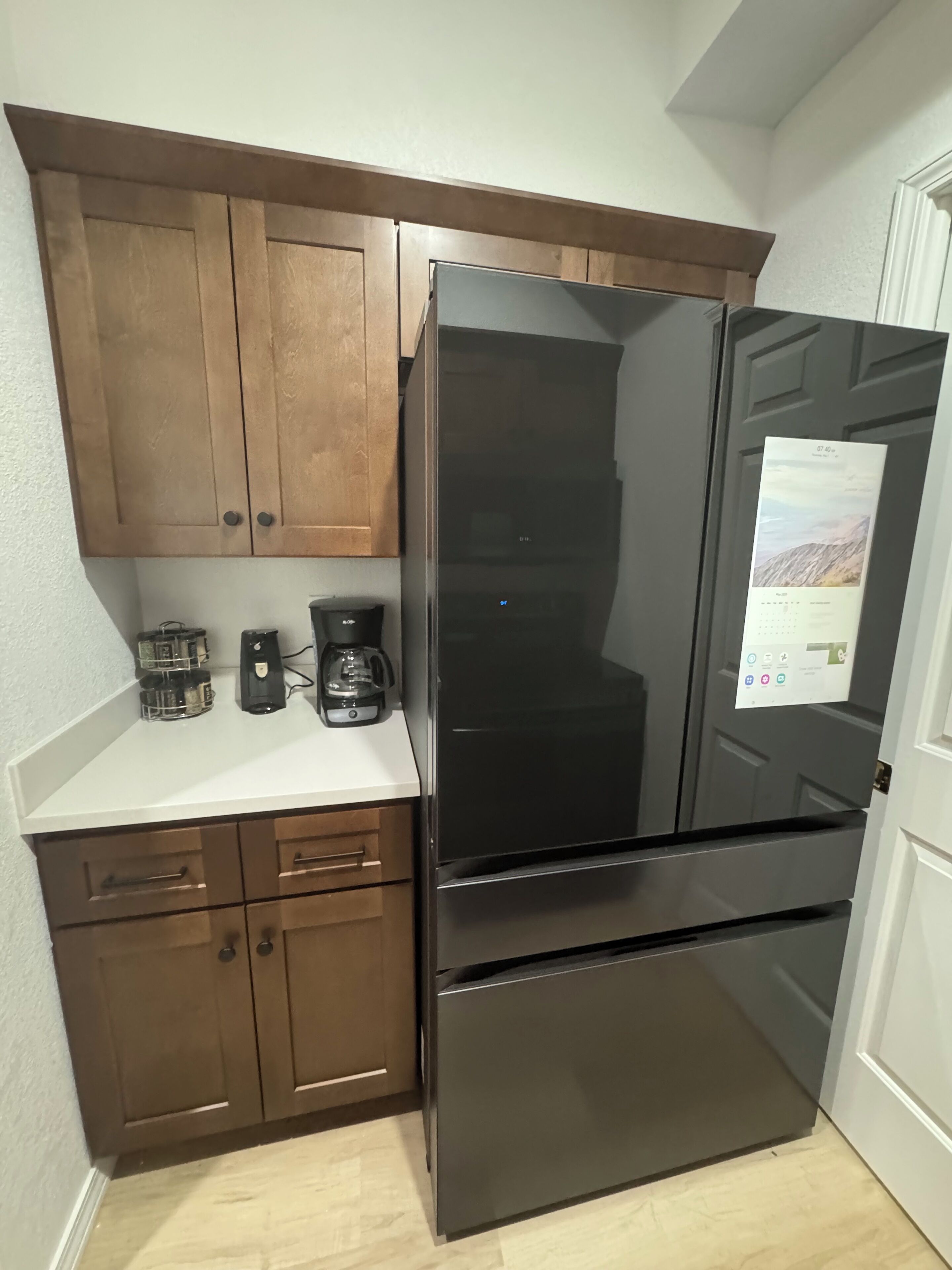 A kitchen with a black refrigerator, wooden cabinets, a white countertop, and a coffee maker.