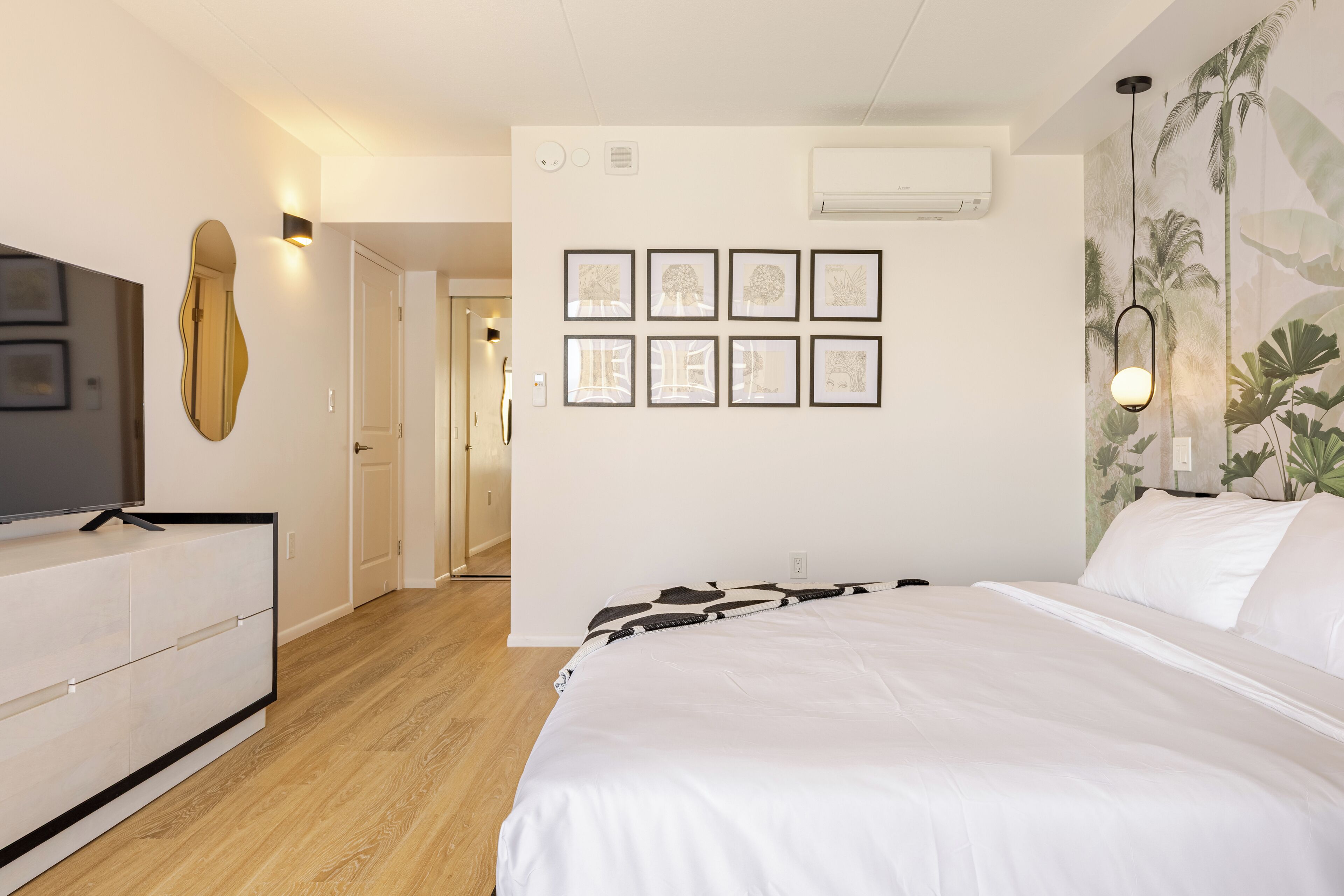 A bedroom with a bed, a dresser, a mirror, and framed artwork on the wall.