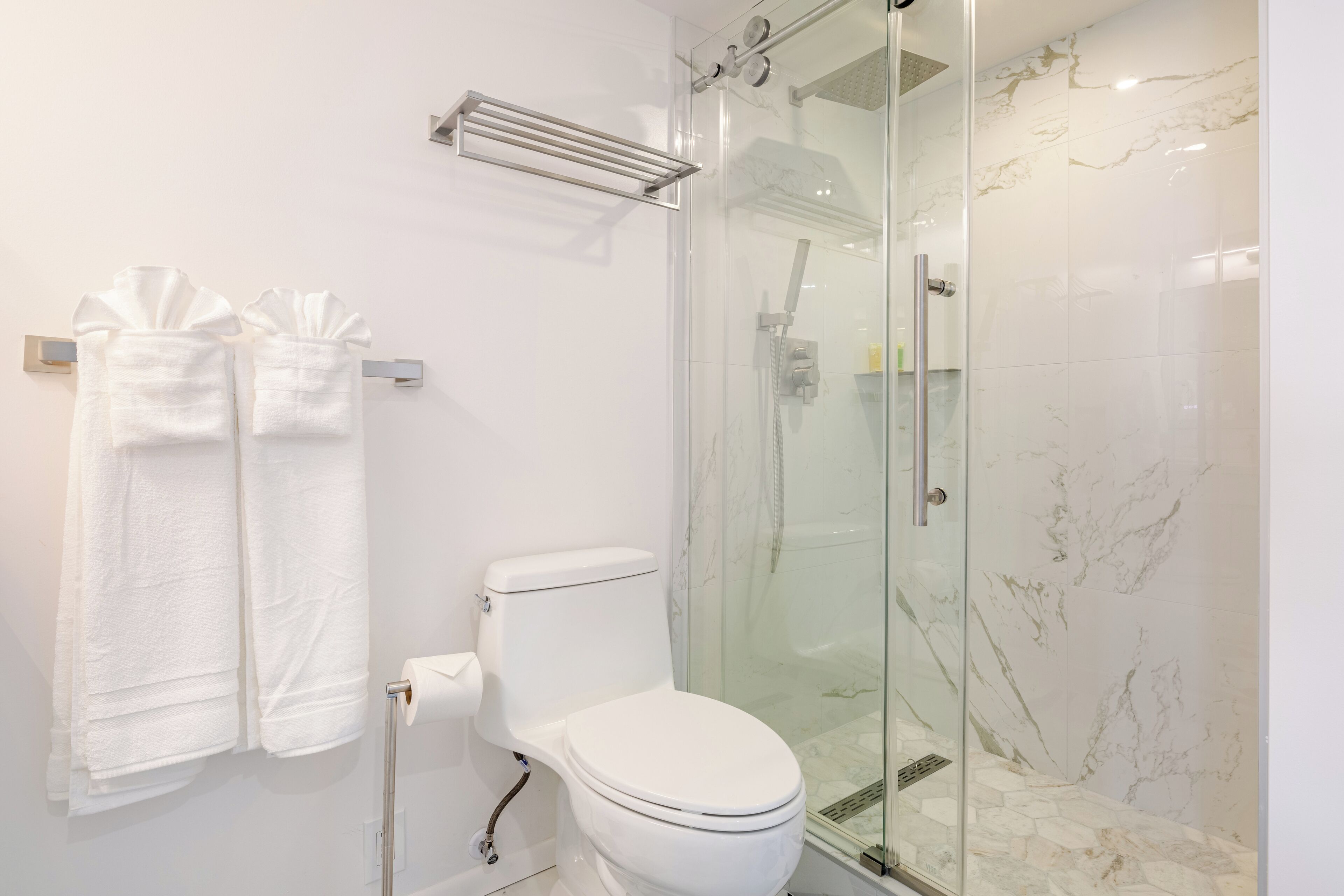 A modern bathroom with a glass-enclosed shower, a toilet, and two towels hanging on a rack.