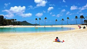 Een strand met helderblauw water, palmbomen en enkele mensen.