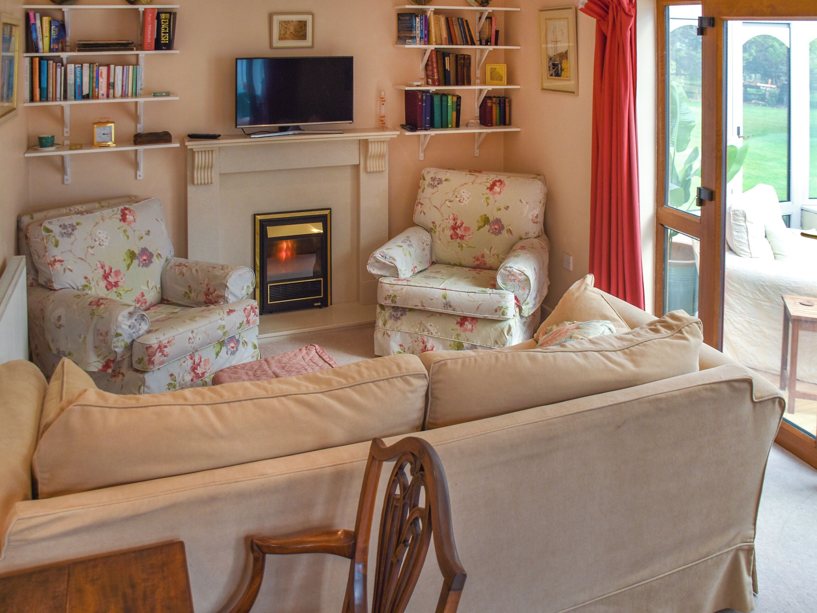 A cozy living room with a fireplace, floral armchairs, a sofa, and a television.