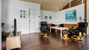 A modern living room with a wooden ceiling, a fireplace, a TV, and a dining area with a table and chairs. - Stunning home in ålbæk with sauna (Ålbæk)