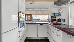 A modern kitchen with white cabinets, a built-in oven, a window with a view, and a clock on the wall. - Stunning home in ålbæk with sauna (Ålbæk)