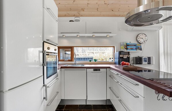 A modern kitchen with white cabinets, a built-in oven, a window with a view, and a clock on the wall.