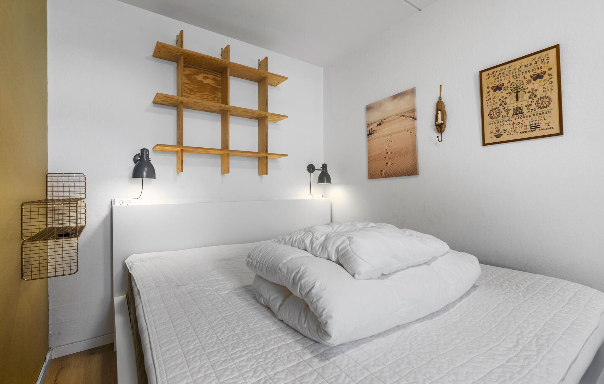 A bedroom with a bed, two wall-mounted lamps, a wooden shelf, and a framed picture.