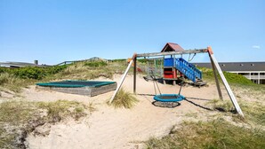 Ein Strandspielplatz mit Schaukeln, einer kleinen Rutsche und einem Trampolin.