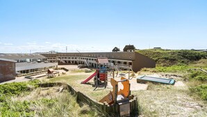 Ein Spielplatz mit Rutschen, Schaukeln, einem Picknicktisch und einem kleinen Gebäude.