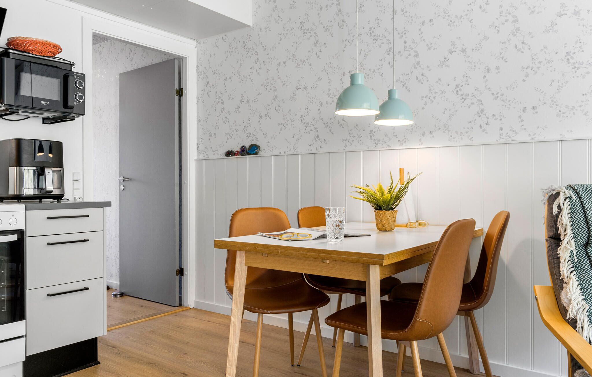 A compact kitchen with a microwave, coffee machine, and a small dining area with a wooden table and chairs.