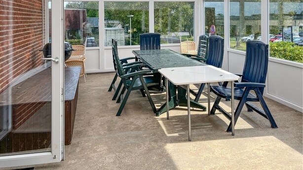 Une terrasse extérieure avec une table et des chaises, de grandes fenêtres et un mur en briques.