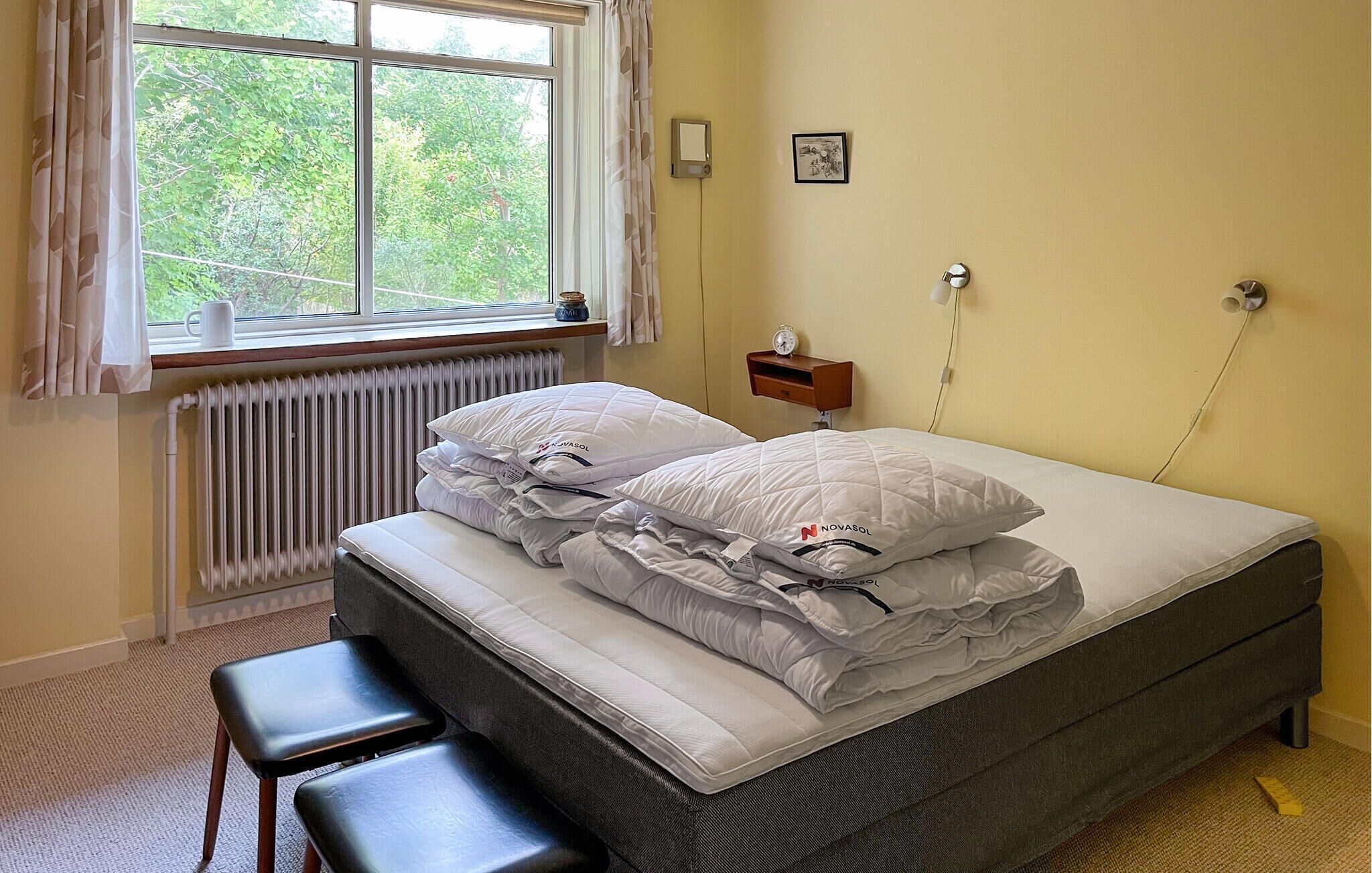 A bedroom with a bed, a bedside table, a window, a radiator, and a picture on the wall.