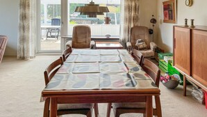 Un espace repas avec une longue table en bois, des chaises rembourrées et une vue sur l’extérieur grâce à de grandes fenêtres.