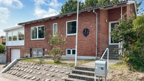 Une maison à deux étages, construite en briques, avec un garage, un porche à l’avant et une boîte aux lettres.